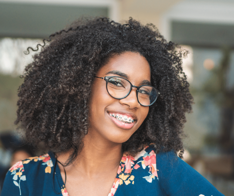 Smiling young woman with braces and glasses, showing her teeth confidently during orthodontic treatment.