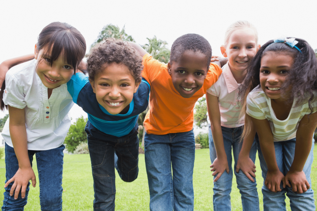 Five smiling children standing together outdoors in a park