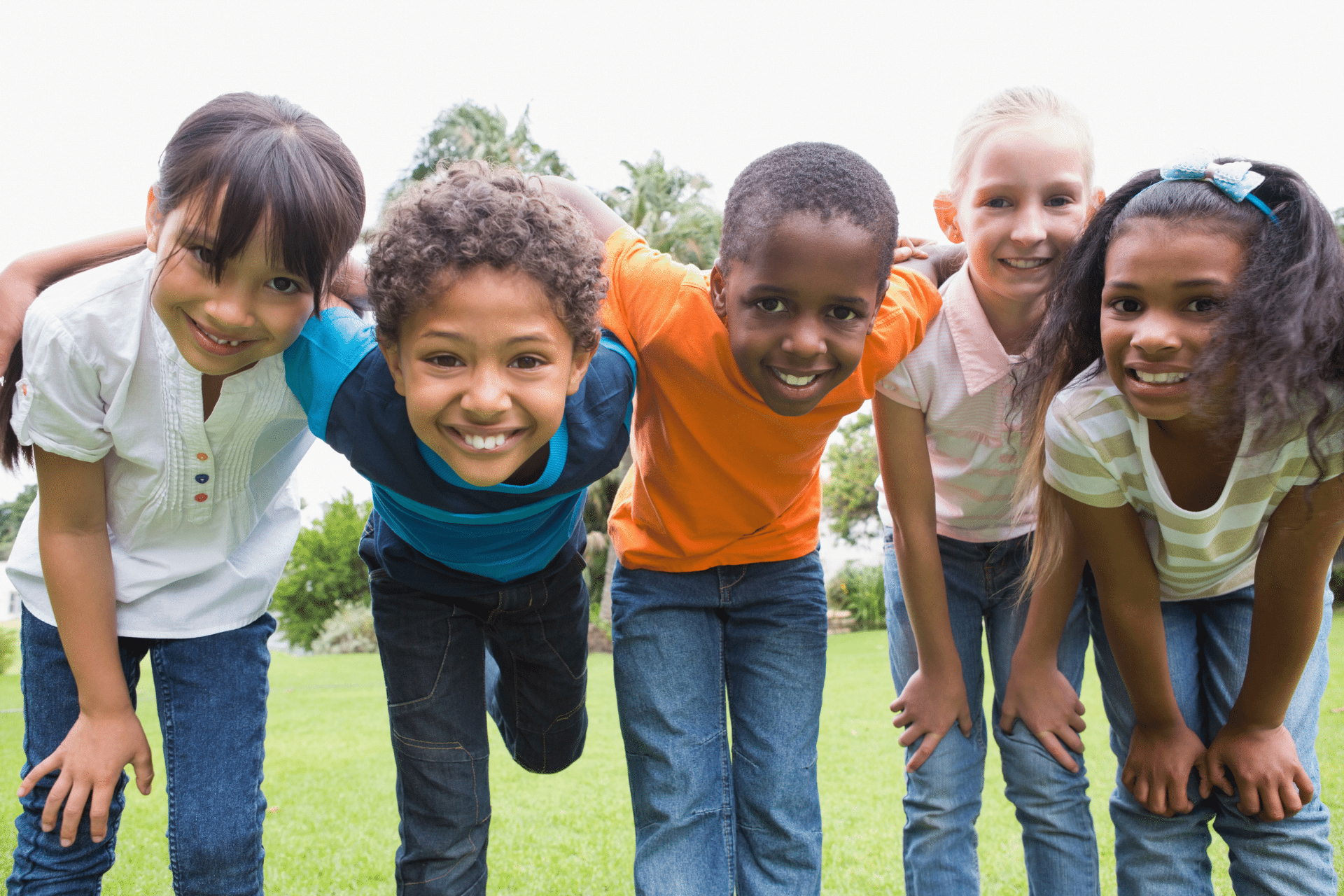 Five smiling children standing together outdoors in a park