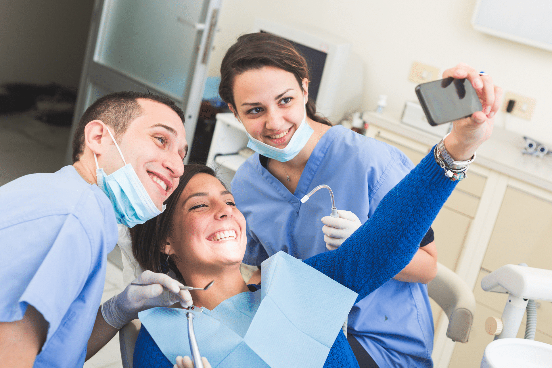 Smiling patient taking a selfie with two dental professionals in a clinic setting